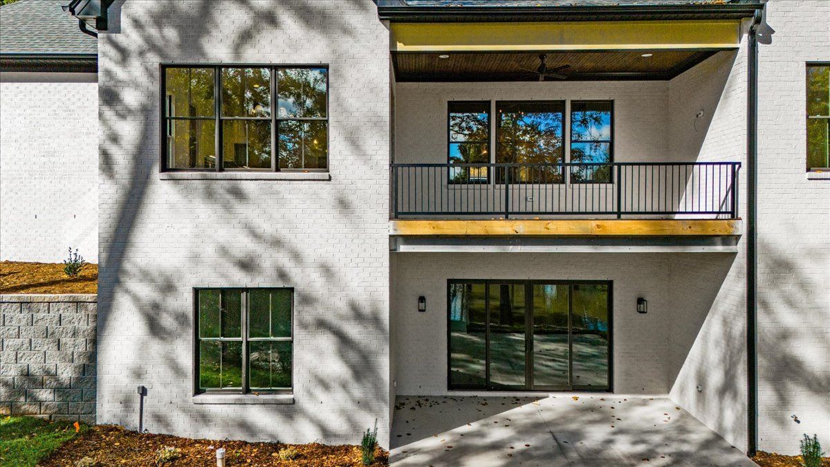 White brick house exterior with a balcony and dark-framed windows.
