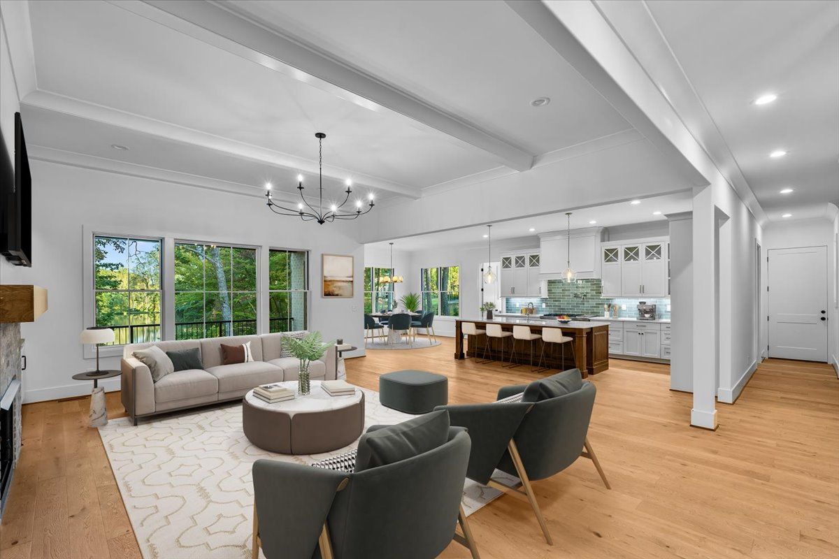 Living room with light wood floors, a sofa, chairs, and a kitchen visible in the background.