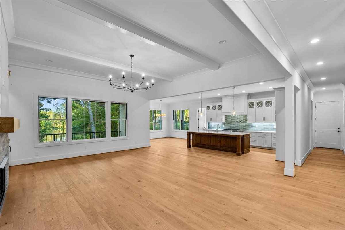 Spacious open-concept living area with light wood floors, white walls, and a large kitchen island.