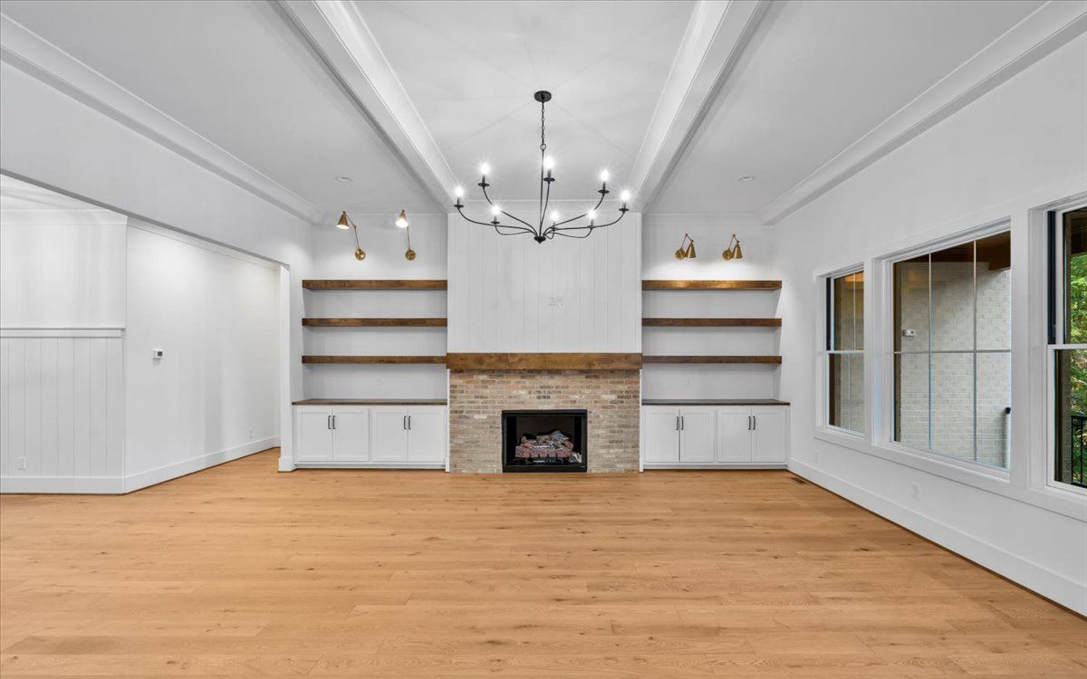 Empty living room with fireplace, built-in shelves, wood floors, and windows.