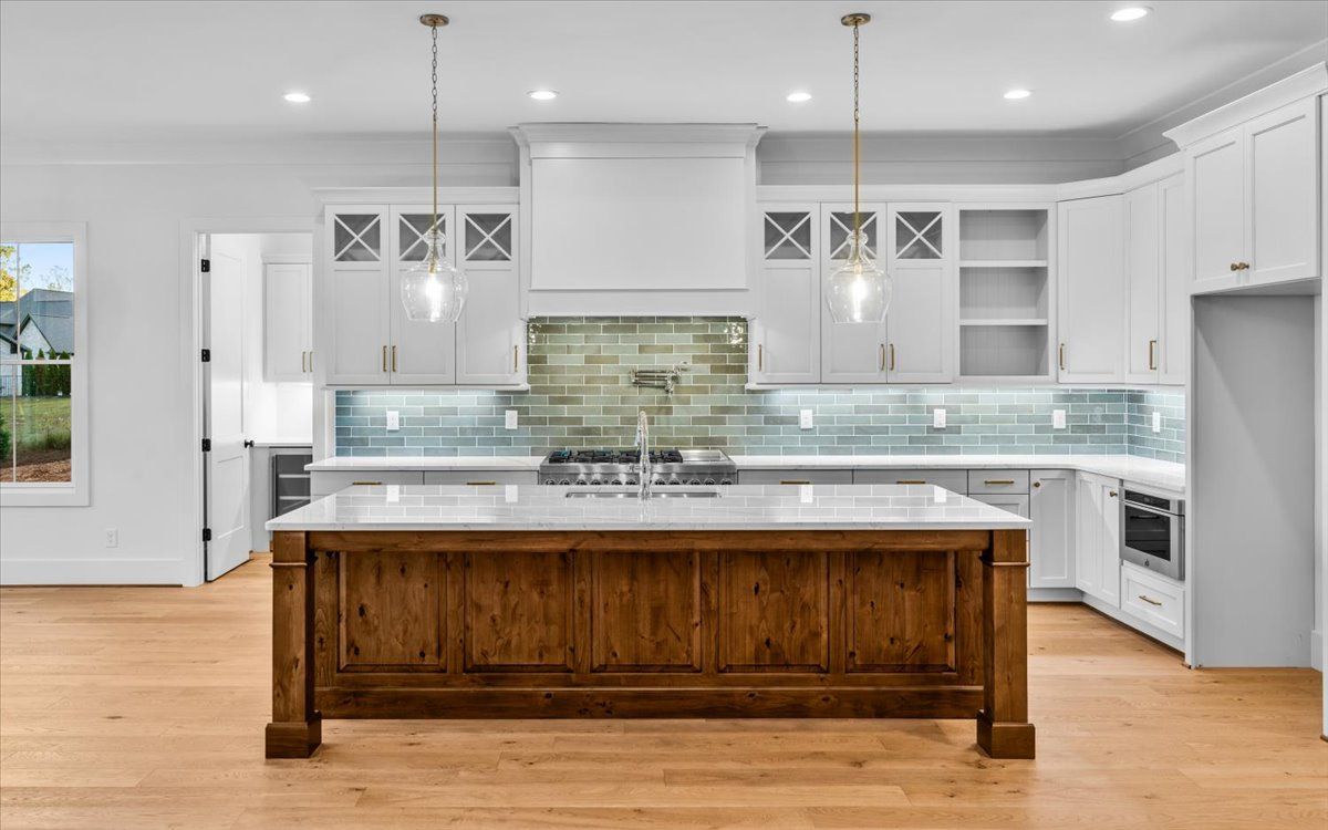 Modern kitchen with a wooden island, white cabinets, and blue tile backsplash.