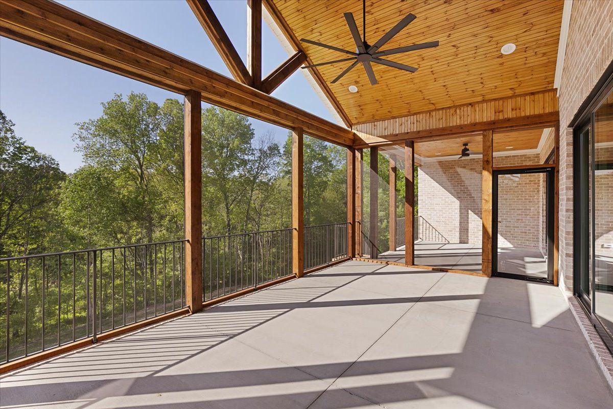 A screened-in porch with a ceiling fan and trees in the background
