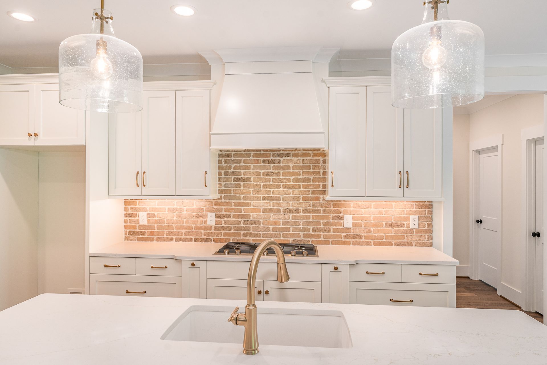 A kitchen with white cabinets, a sink, a stove, and a brick wall