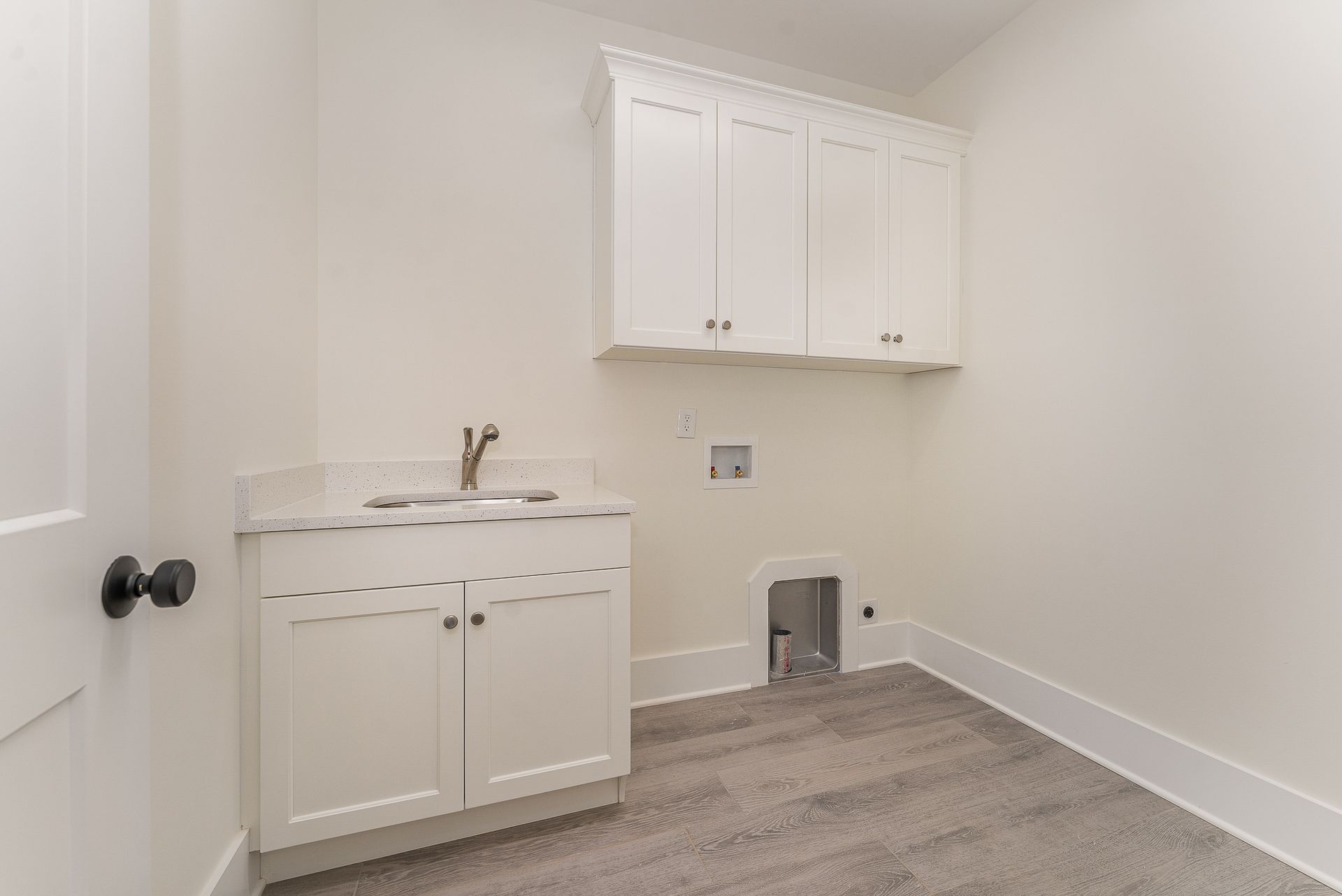 A laundry room with white cabinets and a sink