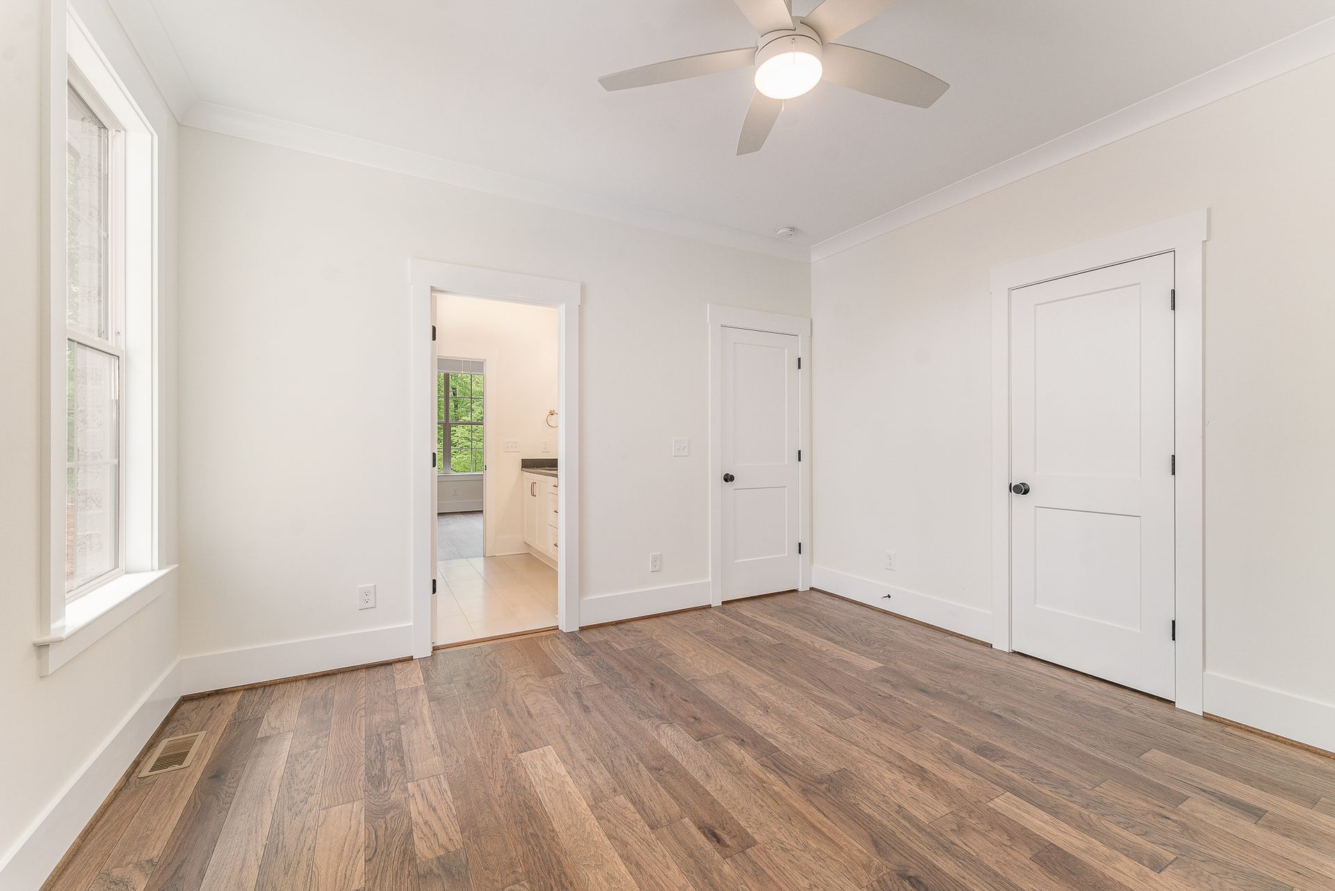 An empty bedroom with hardwood floors and a ceiling fan