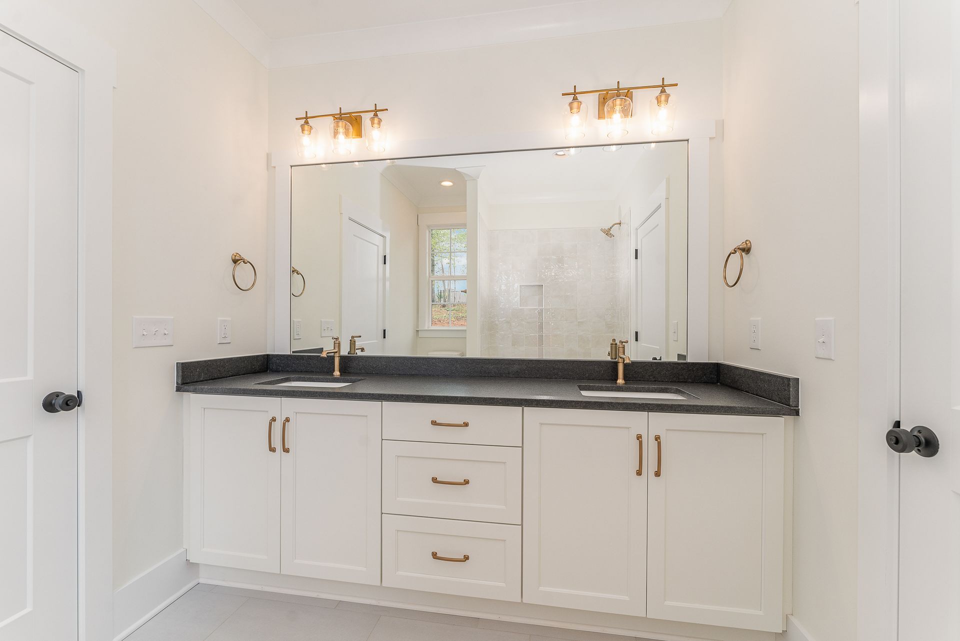 A bathroom with two sinks, light fixtures, and a large mirror