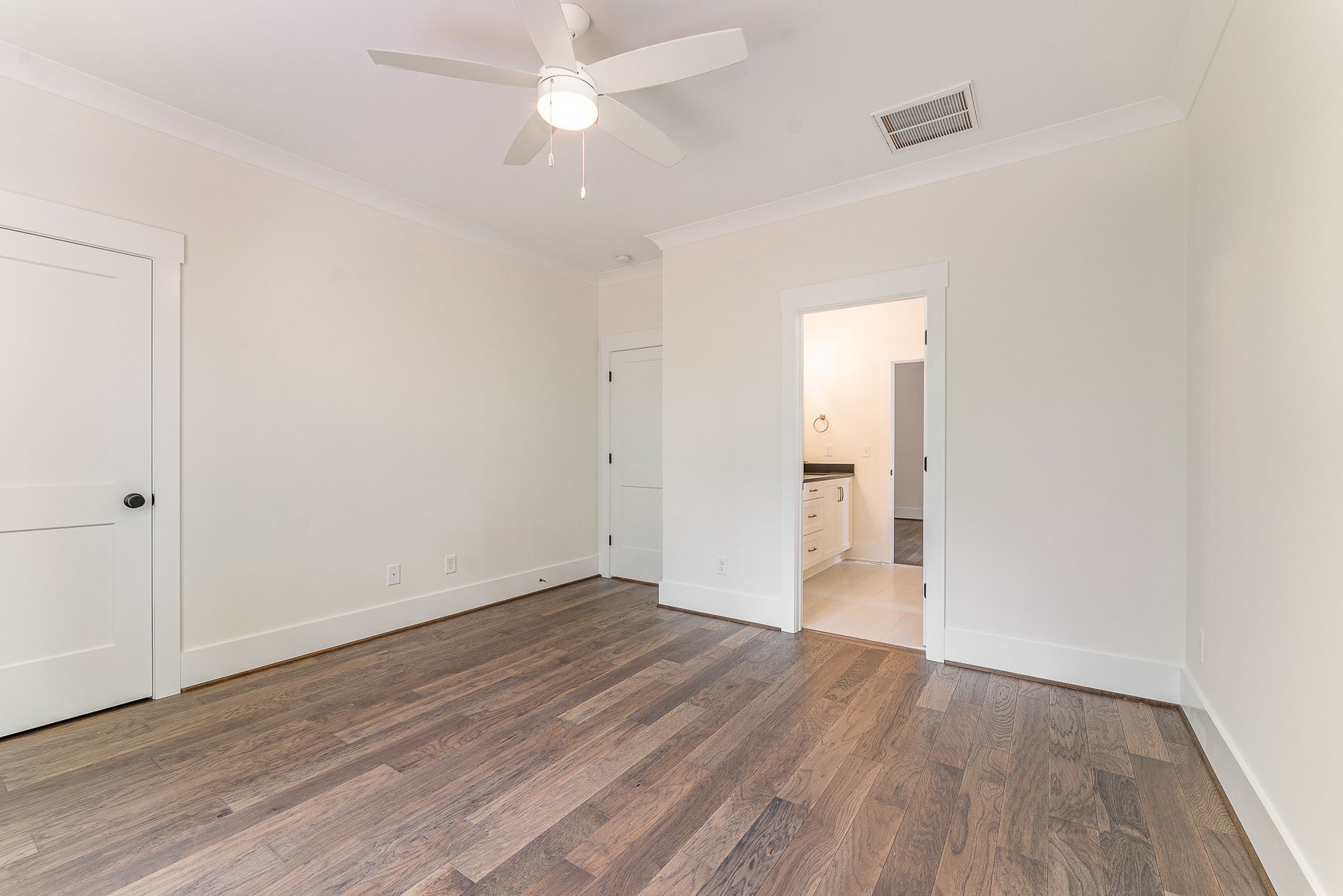 An empty bedroom with hardwood floors and a white ceiling fan