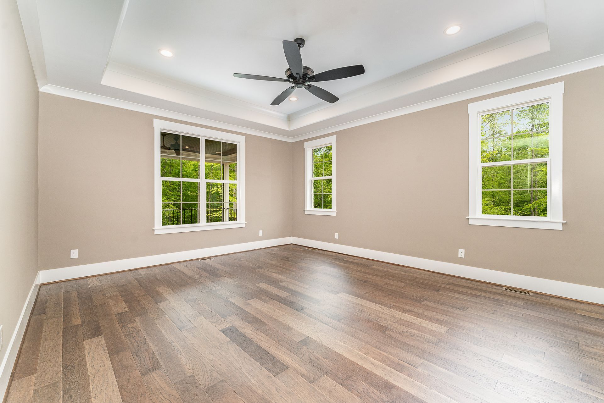 An empty room with three windows and a ceiling fan