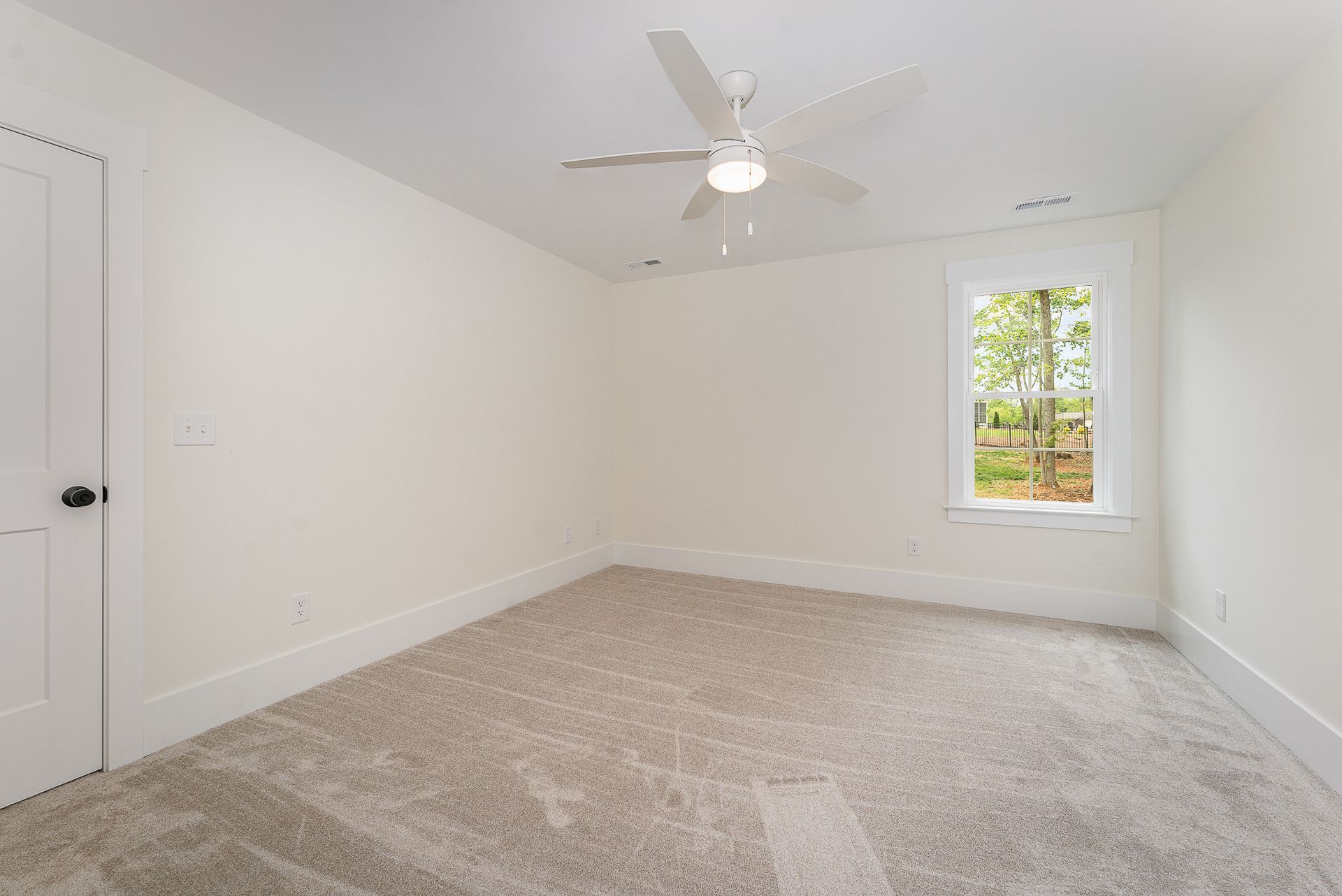 An empty room with a carpeted floor, a ceiling fan, and a window