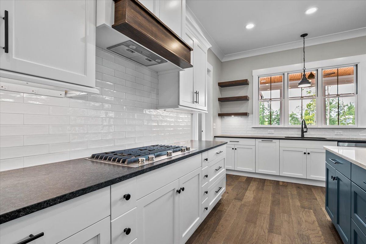 A kitchen with white cabinets, black counter tops, and a stove-top oven