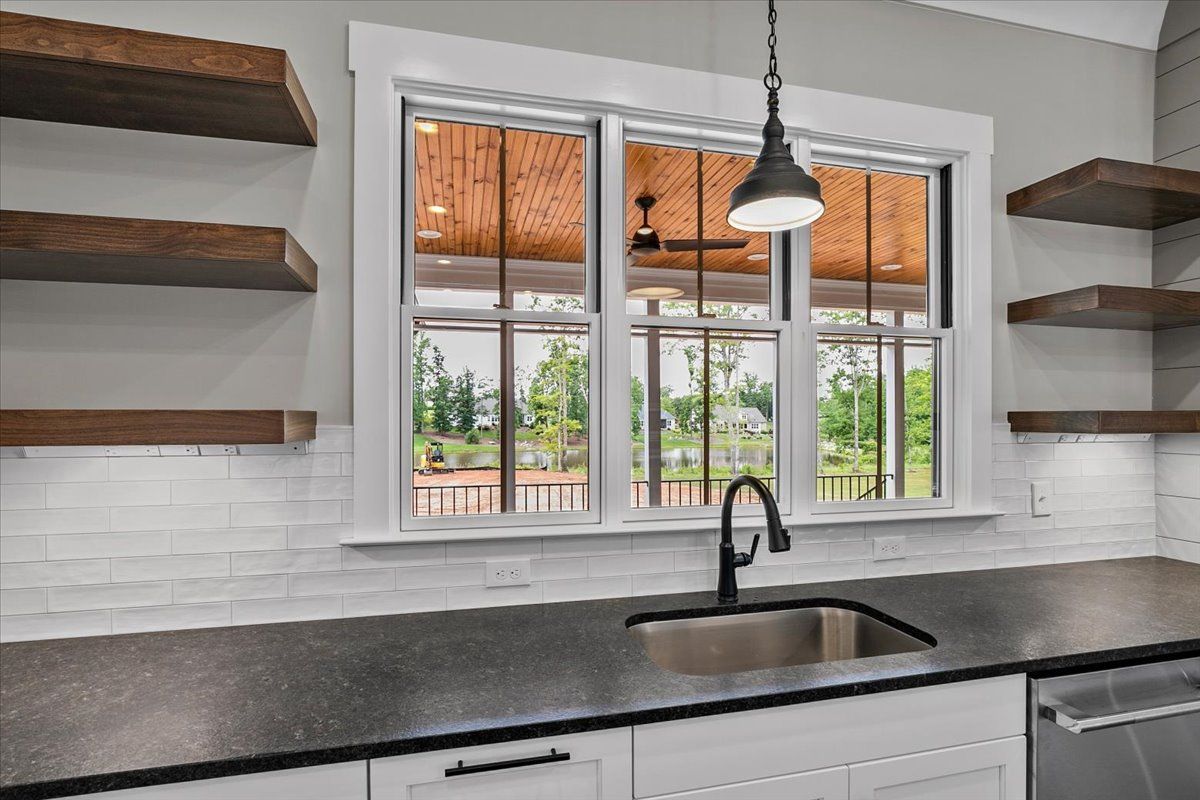 A kitchen with a sink, a large window, and wooden shelves