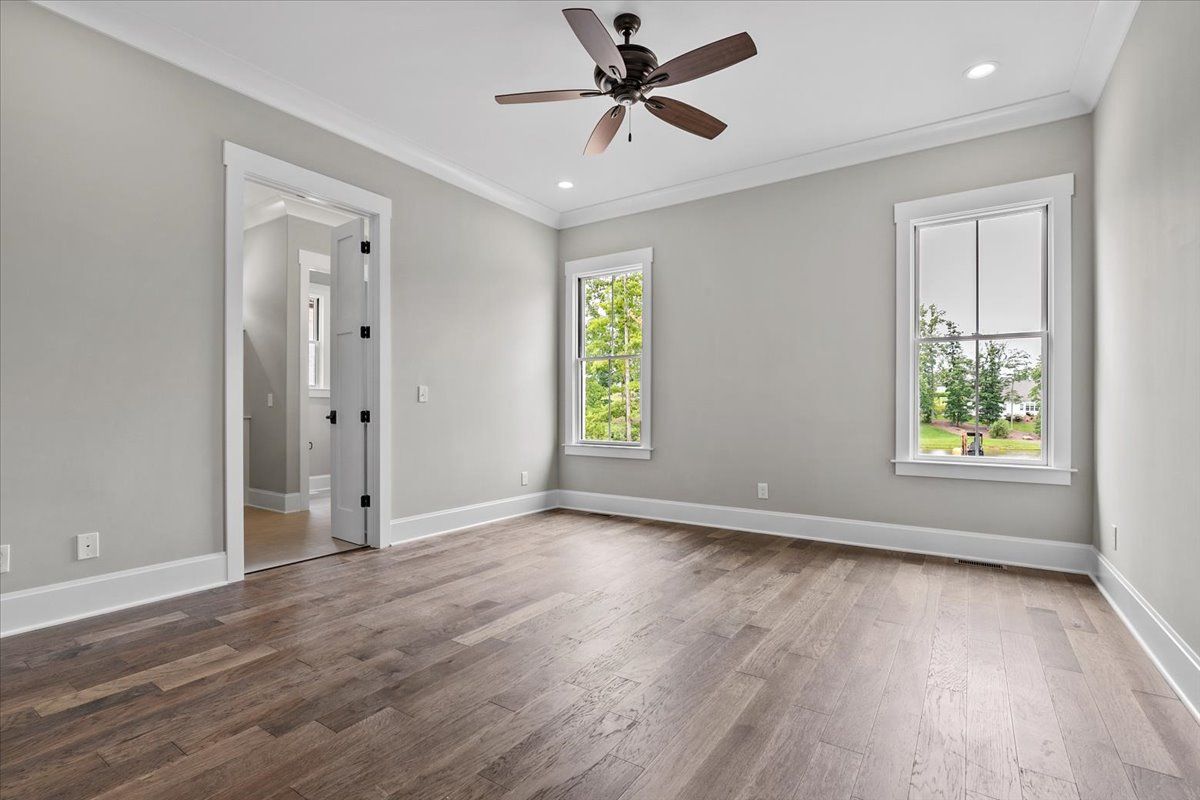 An empty room with hardwood floors, a door, and two windows