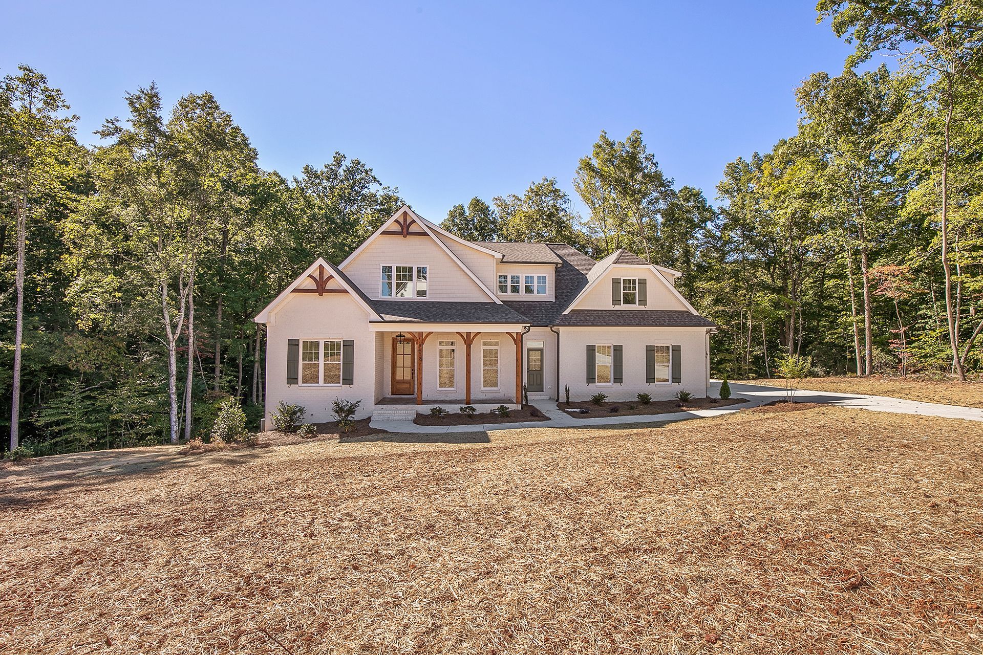 A large white house in the middle of a field surrounded by trees
