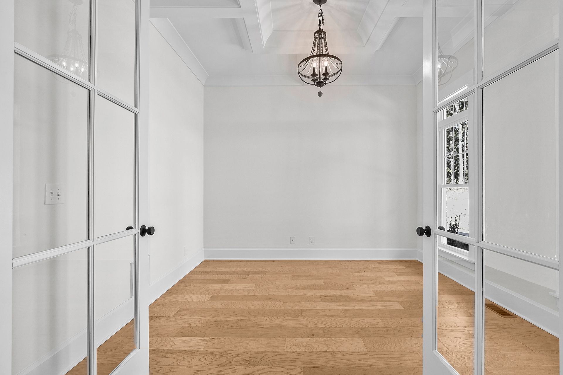 An empty room with hardwood floors and a chandelier hanging from the ceiling