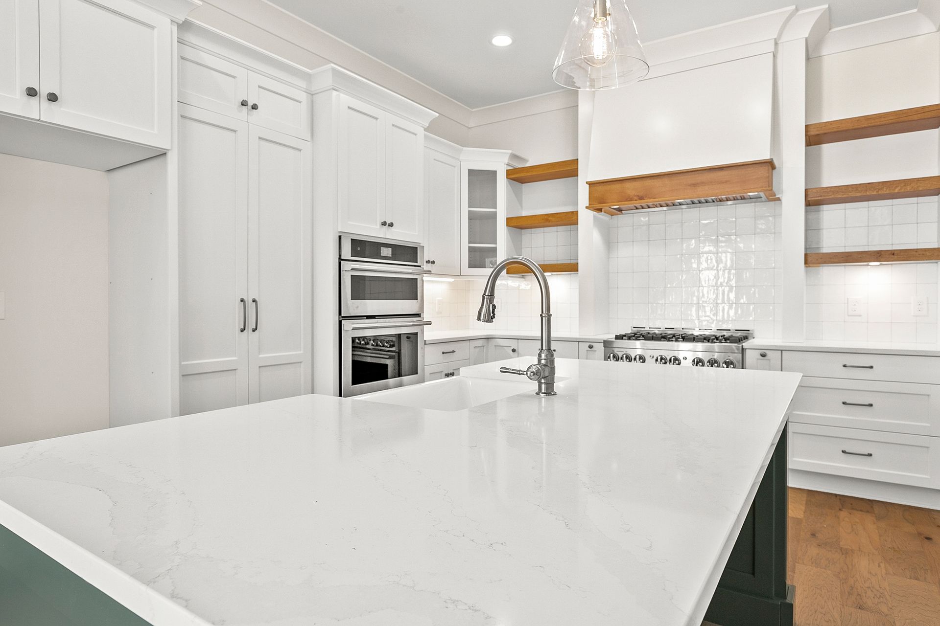 A kitchen with white cabinets, a large island, a sink, and a stove