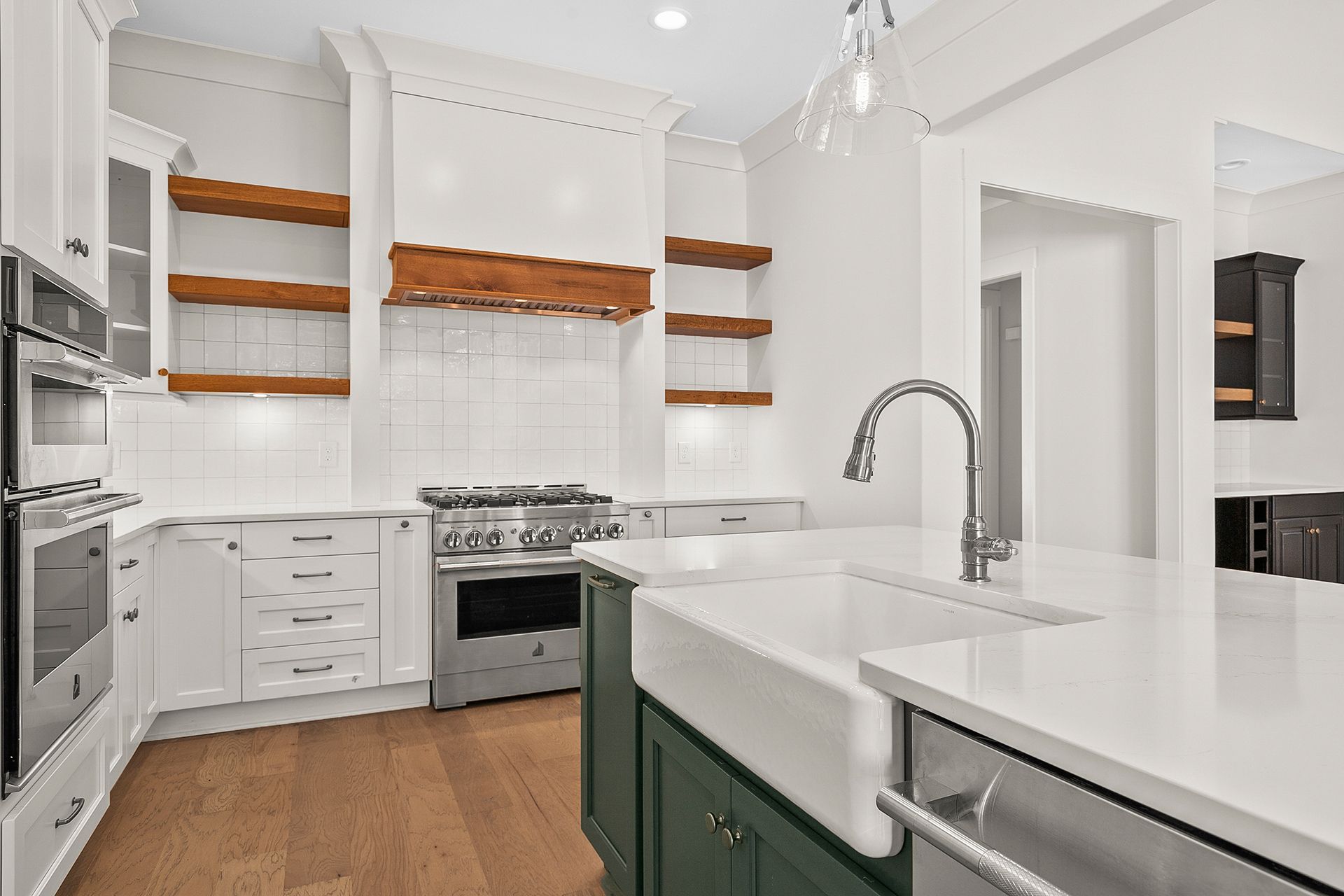 A kitchen with green cabinets, a white sink, stainless steel appliances, and wooden shelves