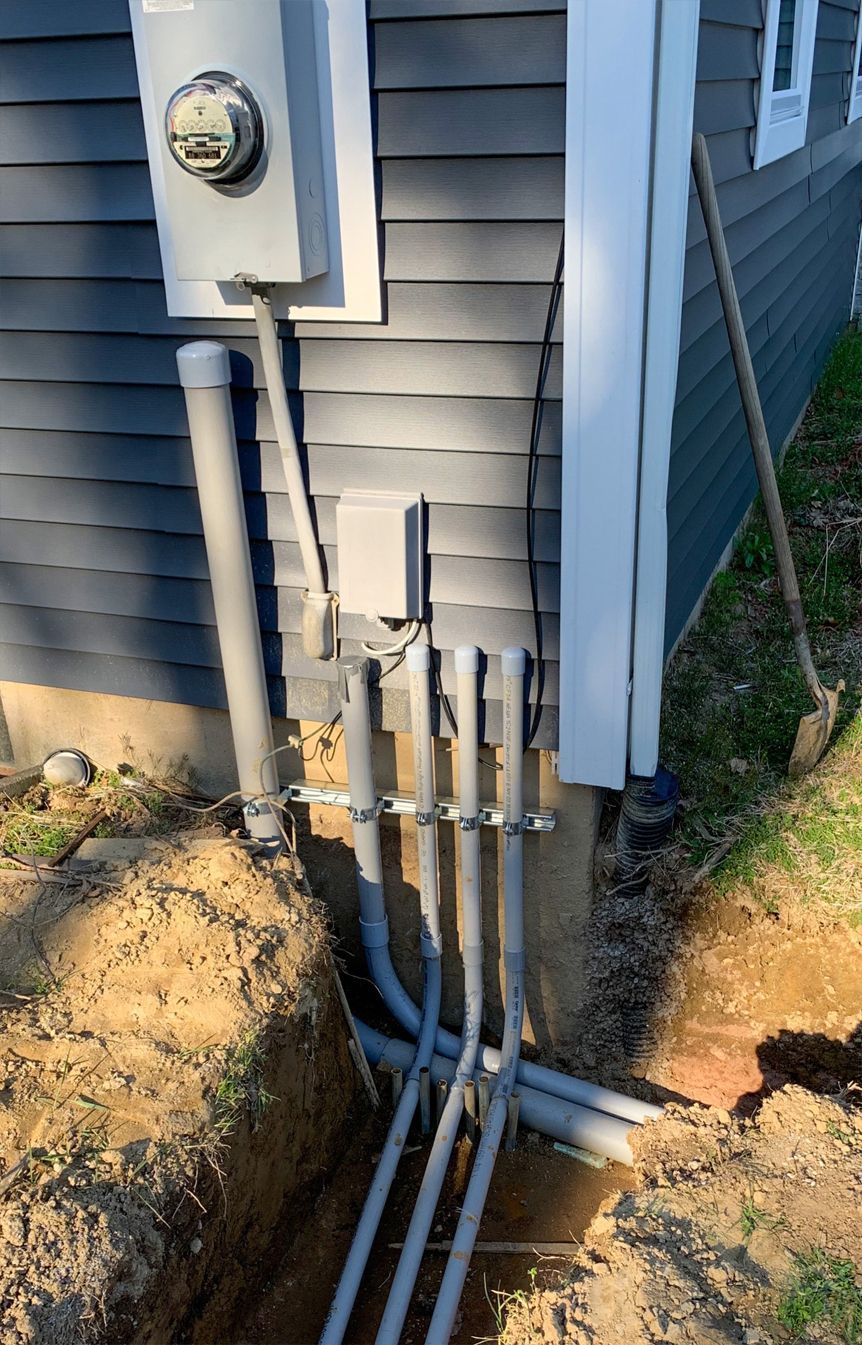 A bunch of electrical wires are coming out of the ground next to a house