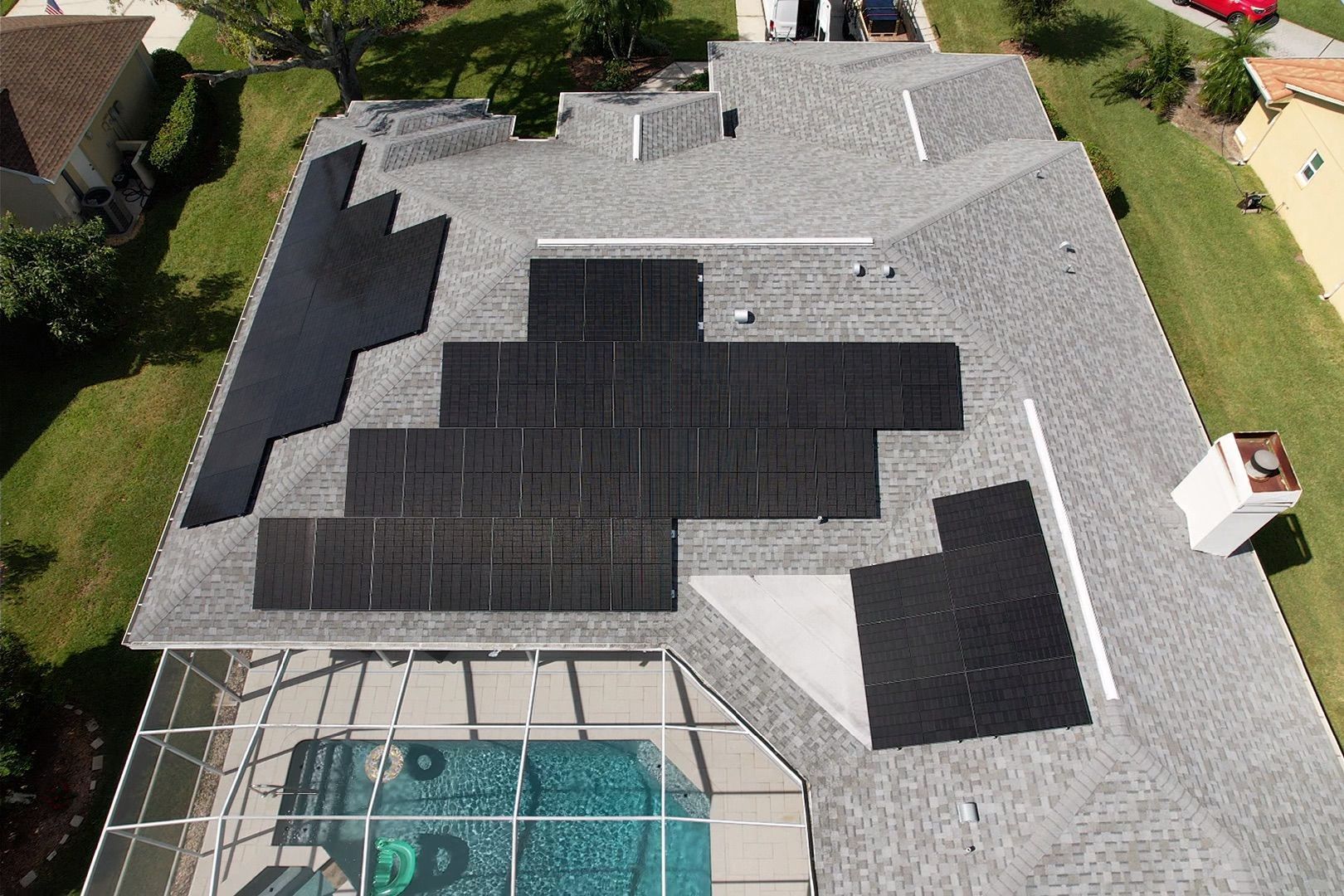Aerial view of a house roof with solar panels and a backyard pool enclosure.