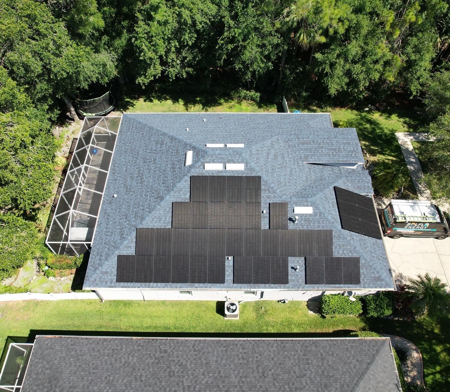 Aerial view of a house roof with solar panels and trees around it.