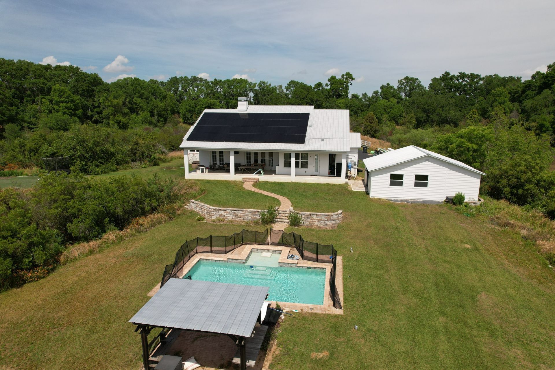 Modern house with solar panels, detached garage, and backyard pool on a grassy hillside.