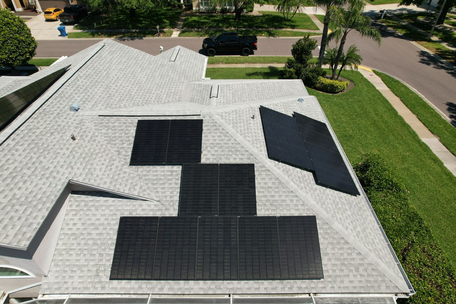Rooftop with multiple black solar panels on a light gray shingle roof in a suburban neighborhood.