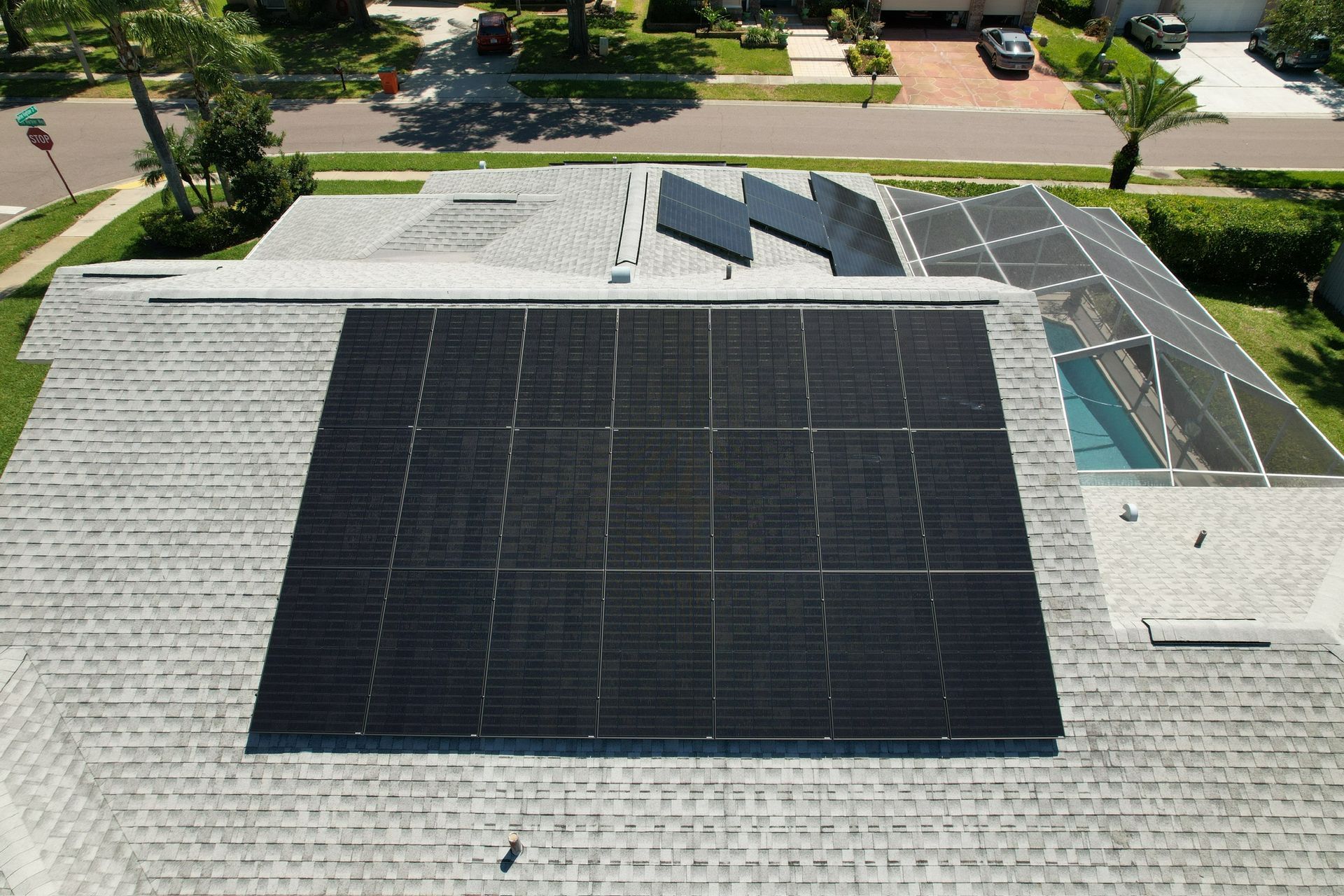 Rooftop solar panels on a gray shingled house, with trees and a street in the background.