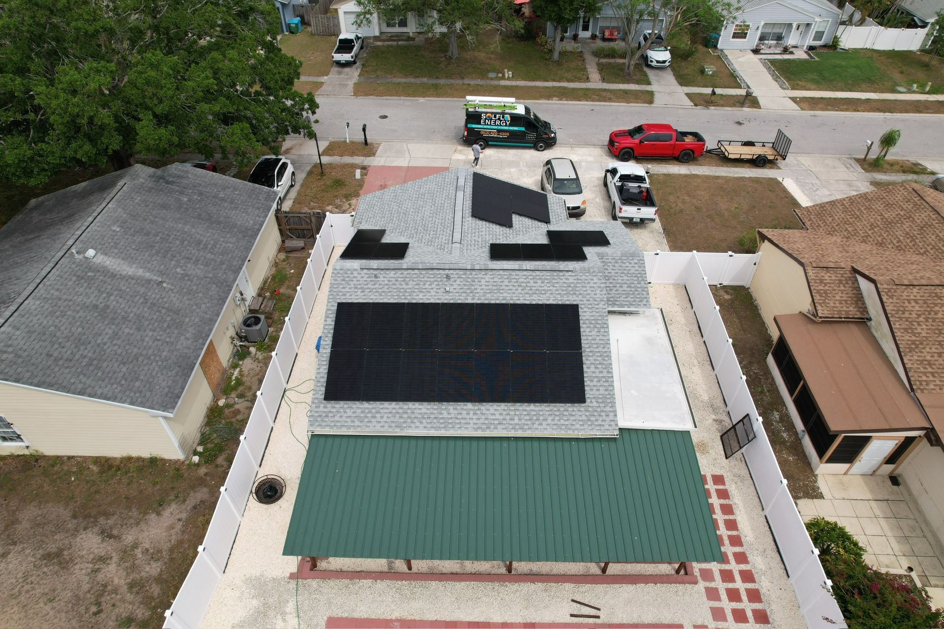 Aerial view of a house roof with solar panels and parked cars on a suburban street.