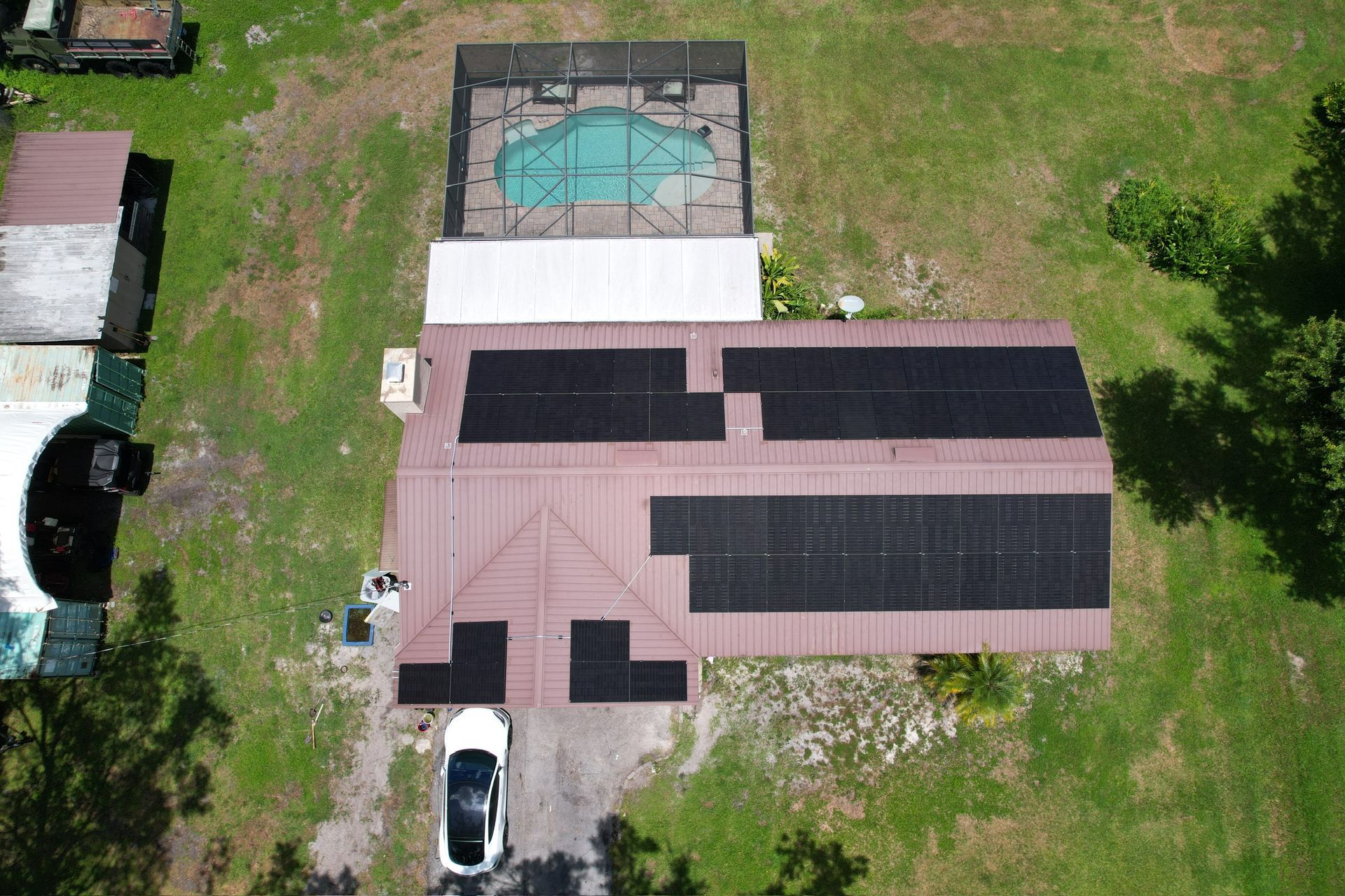 Aerial view of a house roof with solar panels, driveway, parked car, and backyard pool area.