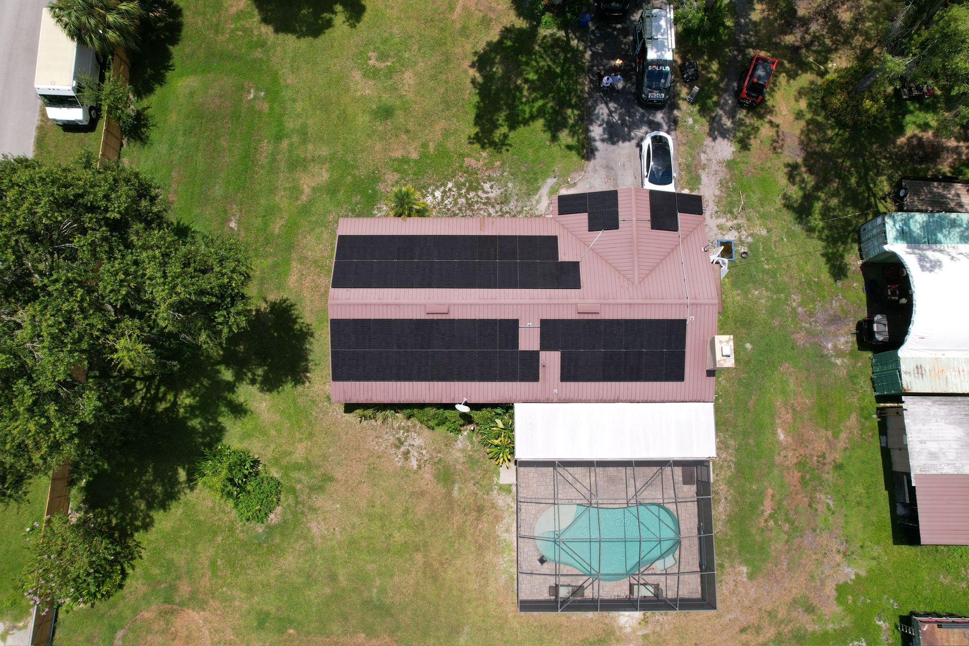 Aerial view of a house with solar panels and a backyard pool surrounded by grass and trees.
