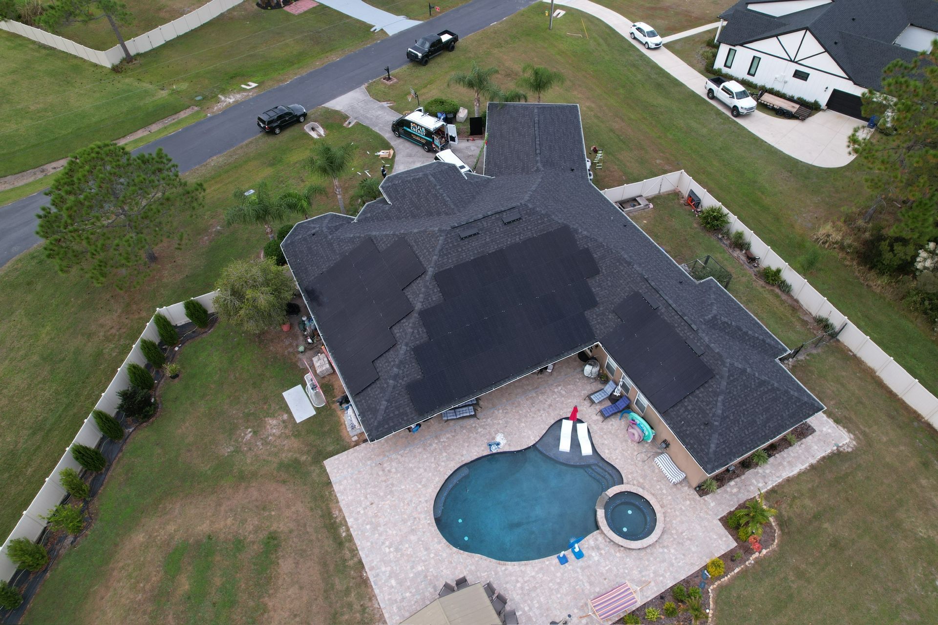 Aerial view of a house with a backyard pool, patio, and driveway in a suburban neighborhood.