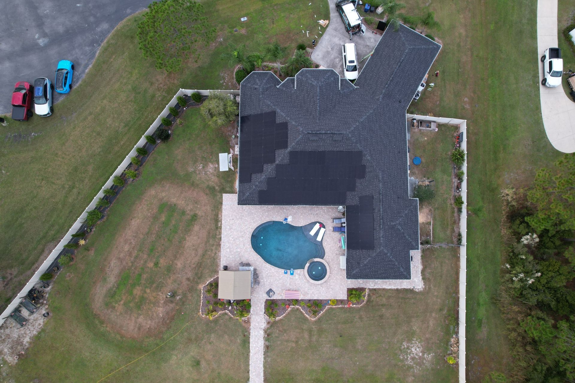 Aerial view of a house with a dark roof, backyard pool, and fenced yard.