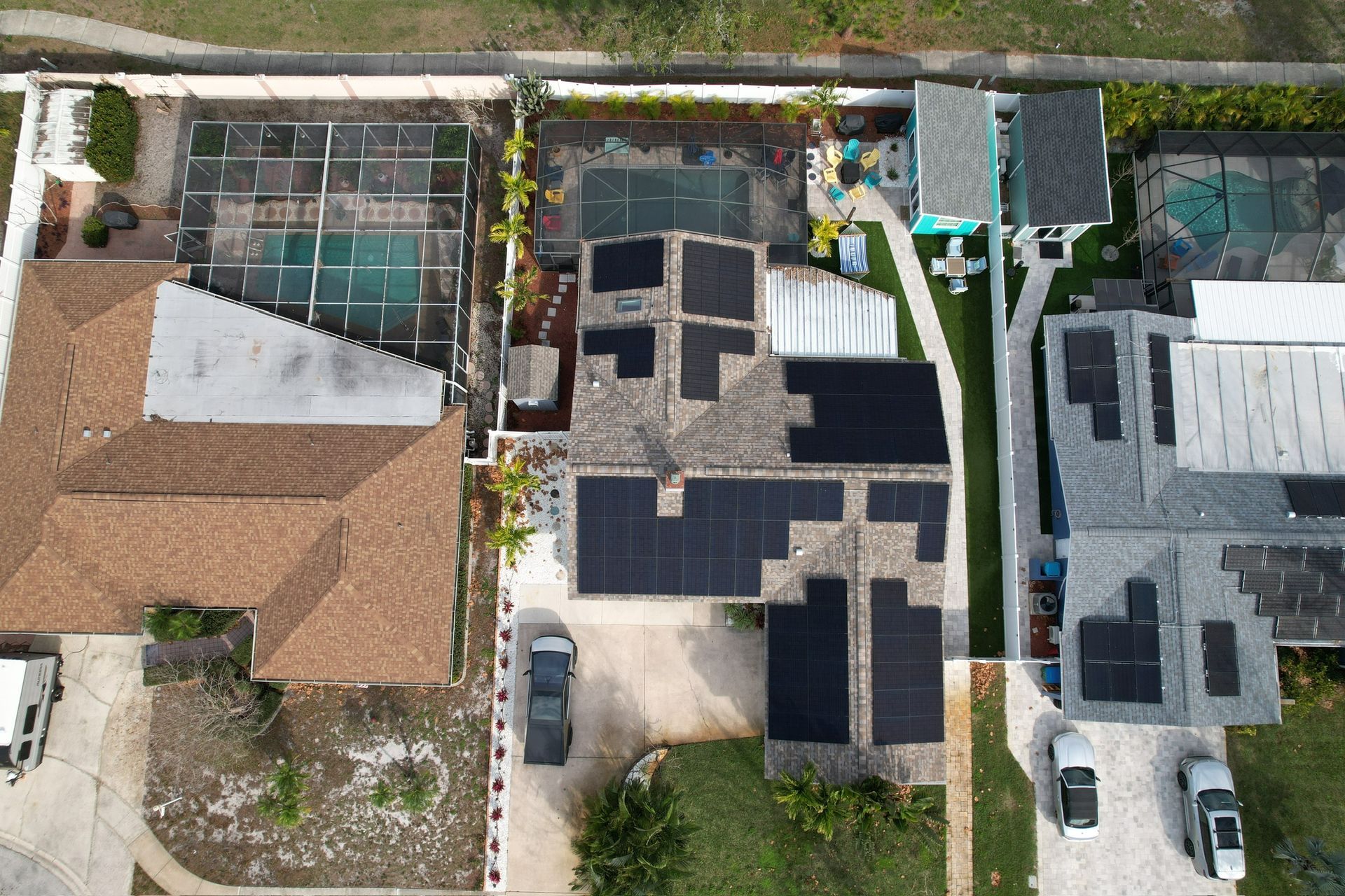 Aerial view of suburban rooftops with solar panels, driveways, and a swimming pool.