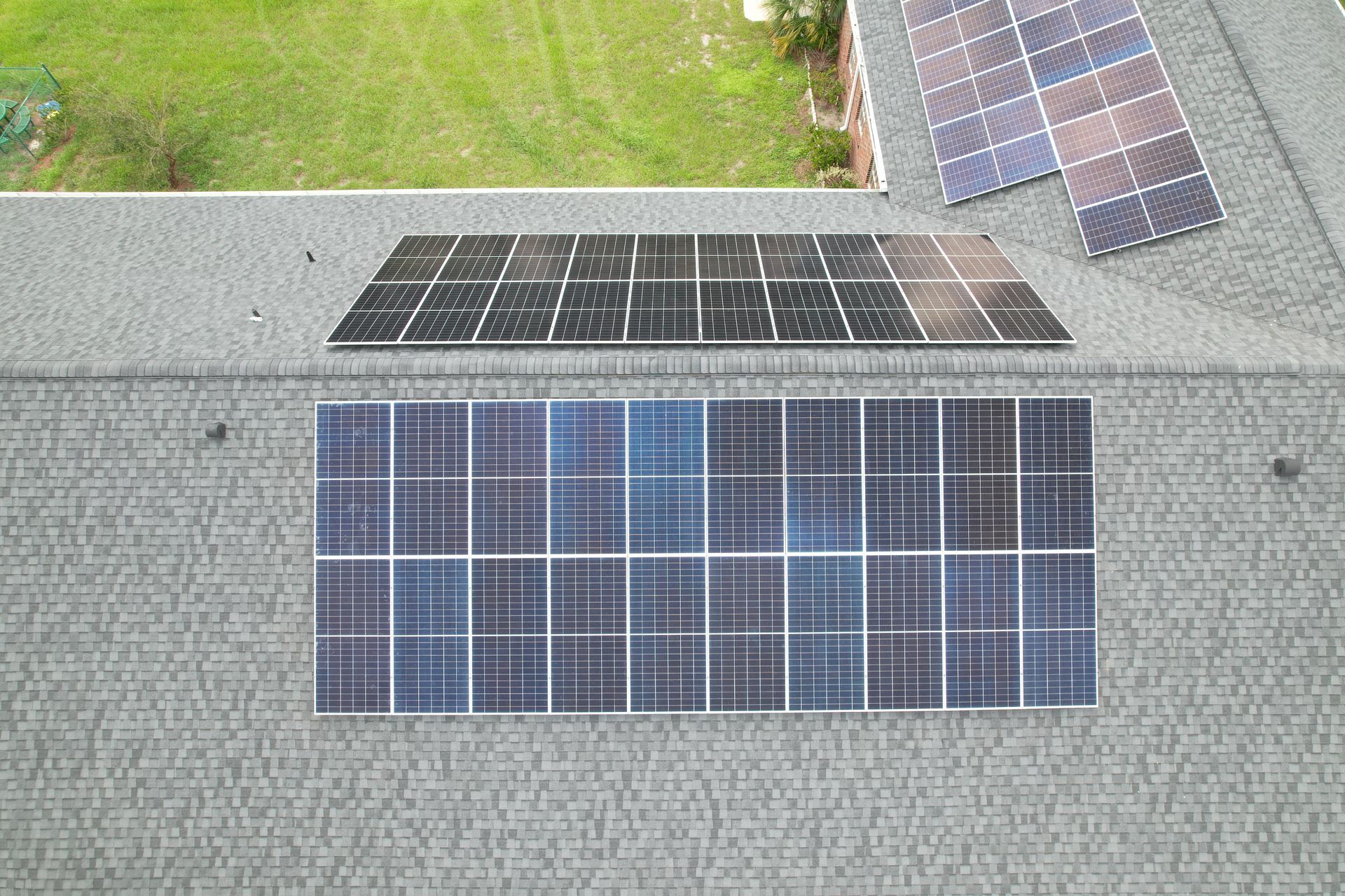 Rooftop solar panels on a shingled roof, with grass and more panels visible above.