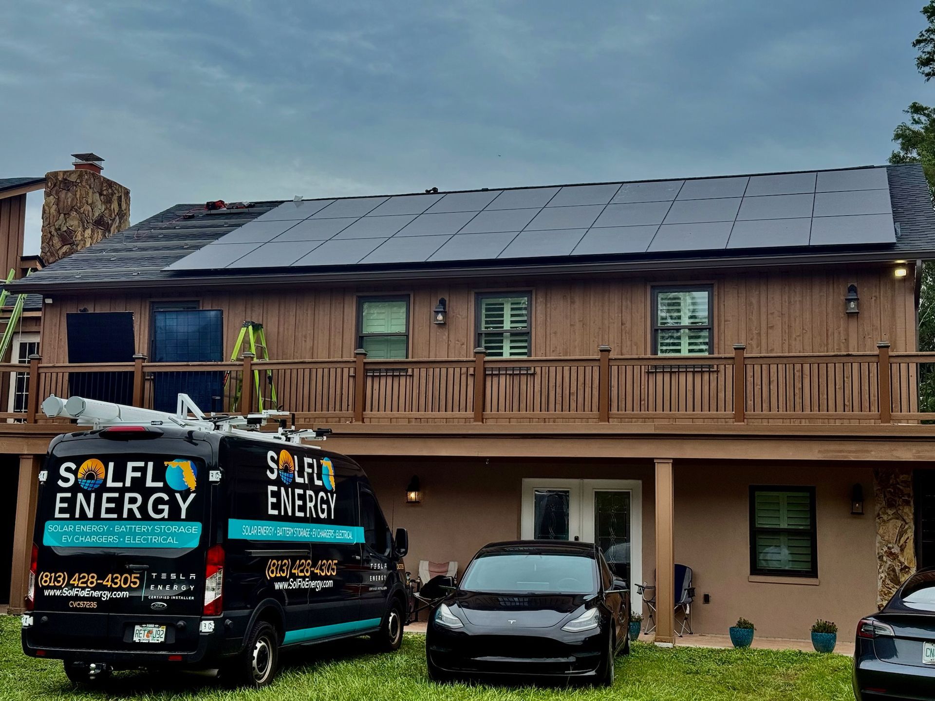 Black house with rooftop solar panels and solar-energy van parked in front.