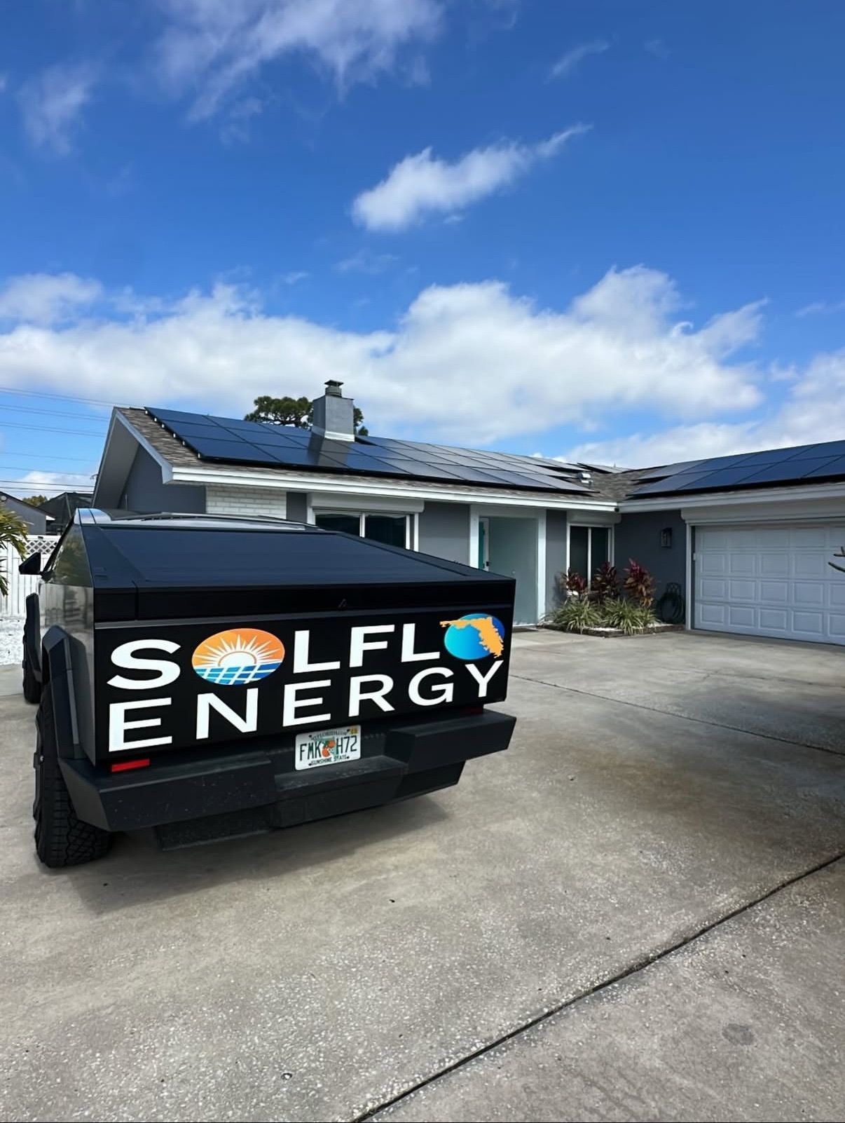 Black SOLEAF Energy dumpster in a residential driveway under a blue sky with clouds.