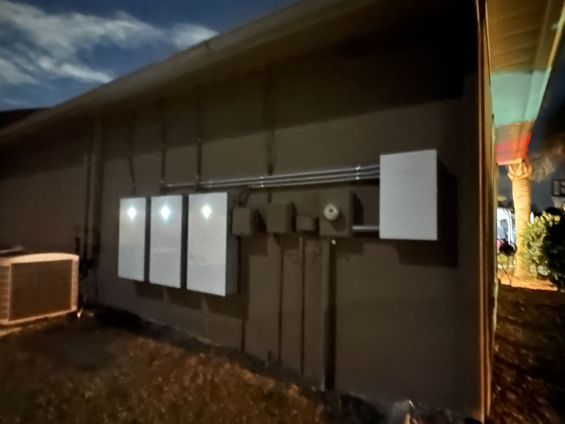 Outdoor wall with electrical panels and meters mounted on a brown building at dusk.