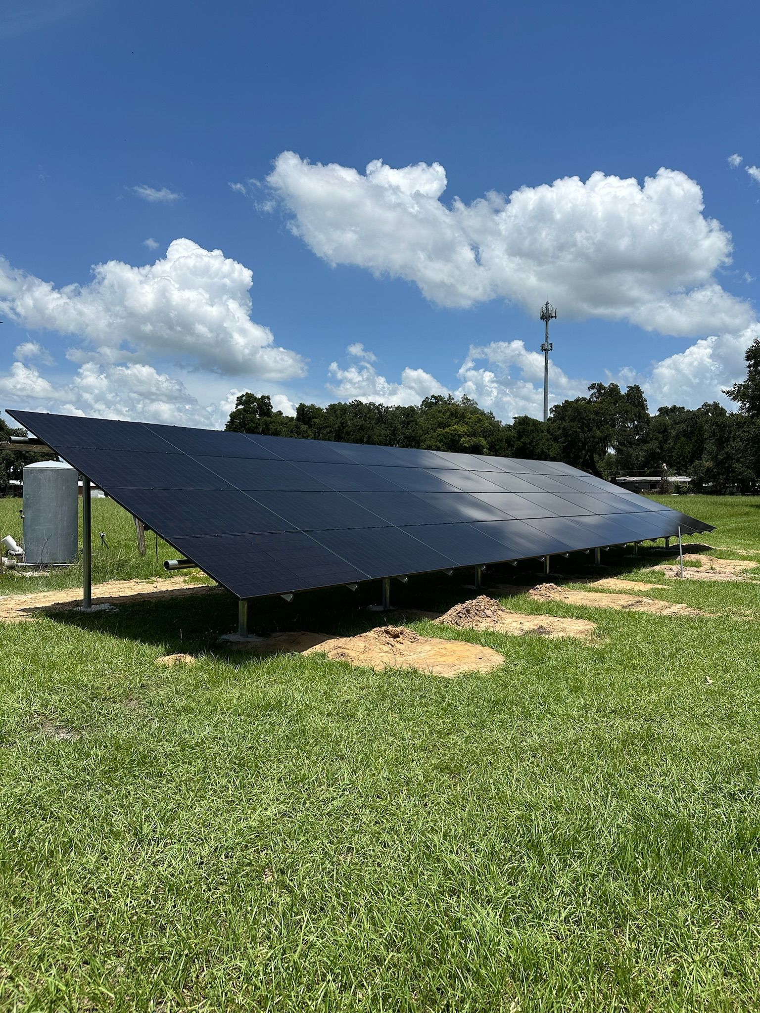 Solar panels on a grassy field under a blue sky with scattered clouds.