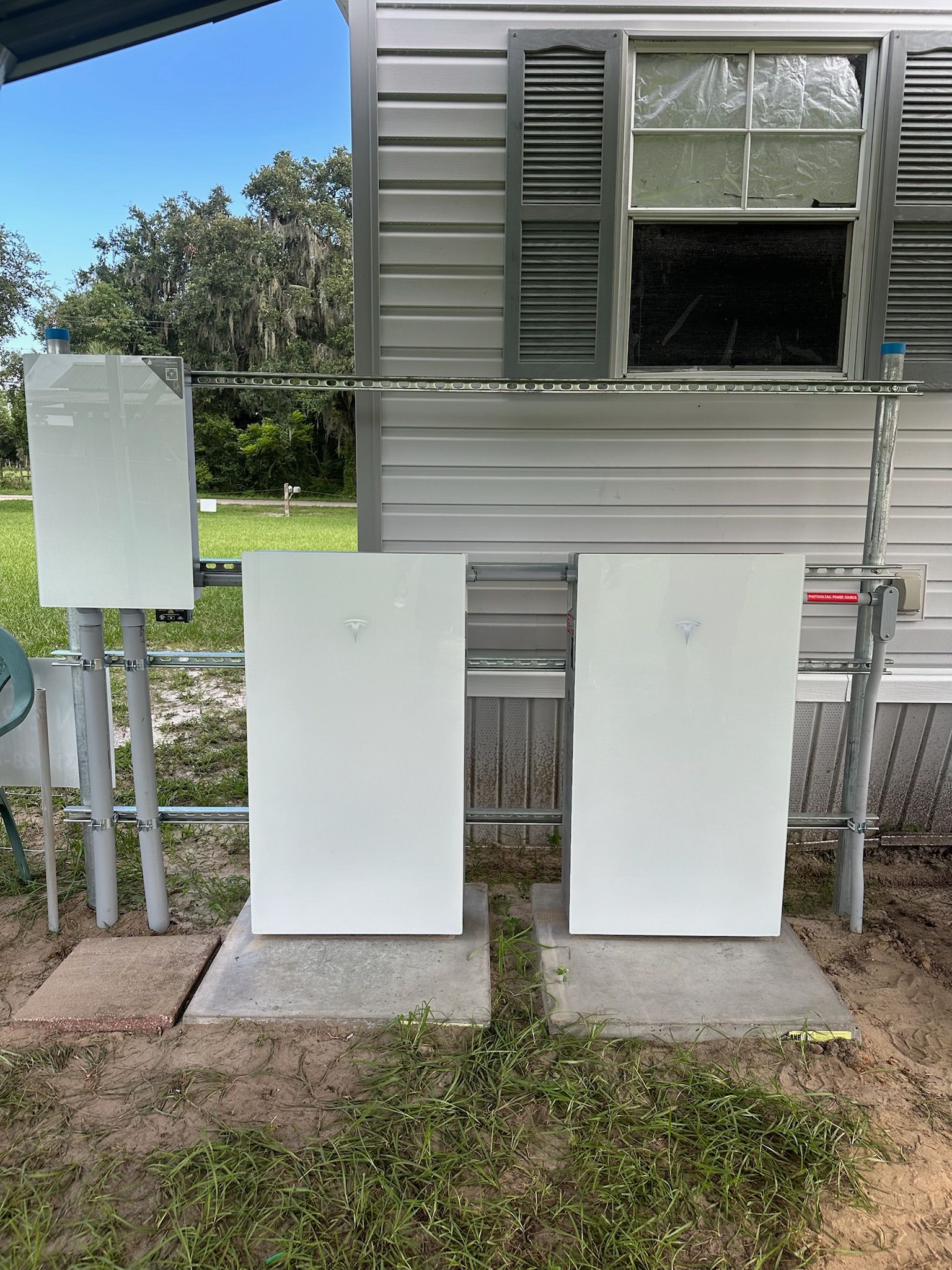 Three white utility boxes beside a small house, with a signpost and window shutters nearby.