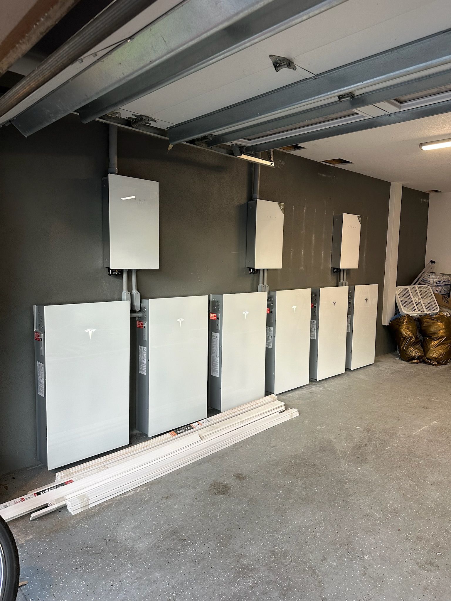 Row of gray electrical cabinets mounted along a garage wall with exposed ceiling beams above.