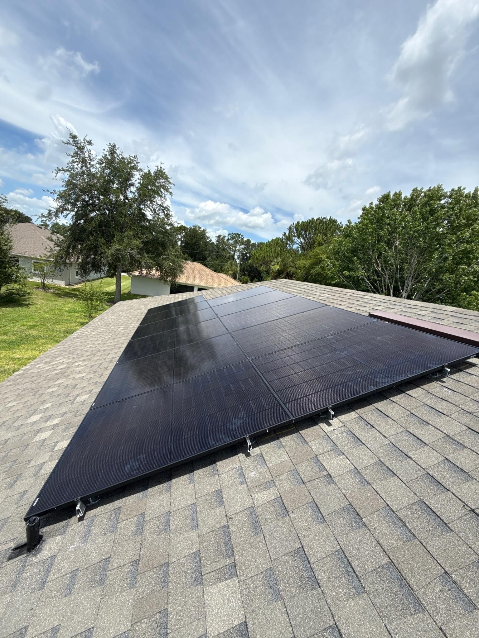 Black solar panels on a sloped roof under a partly cloudy sky.
