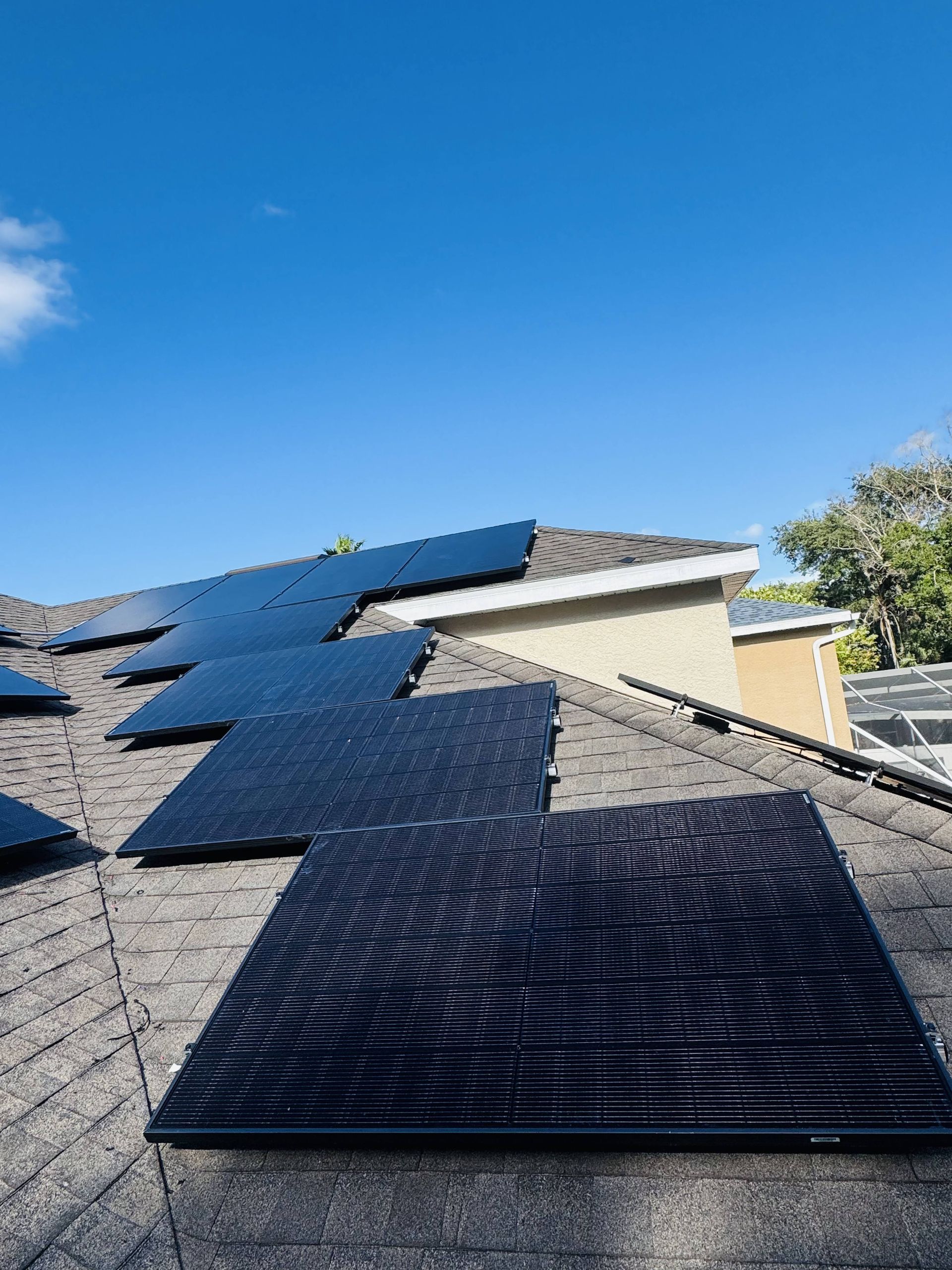 Black solar panels installed on a sloped roof under a clear blue sky.
