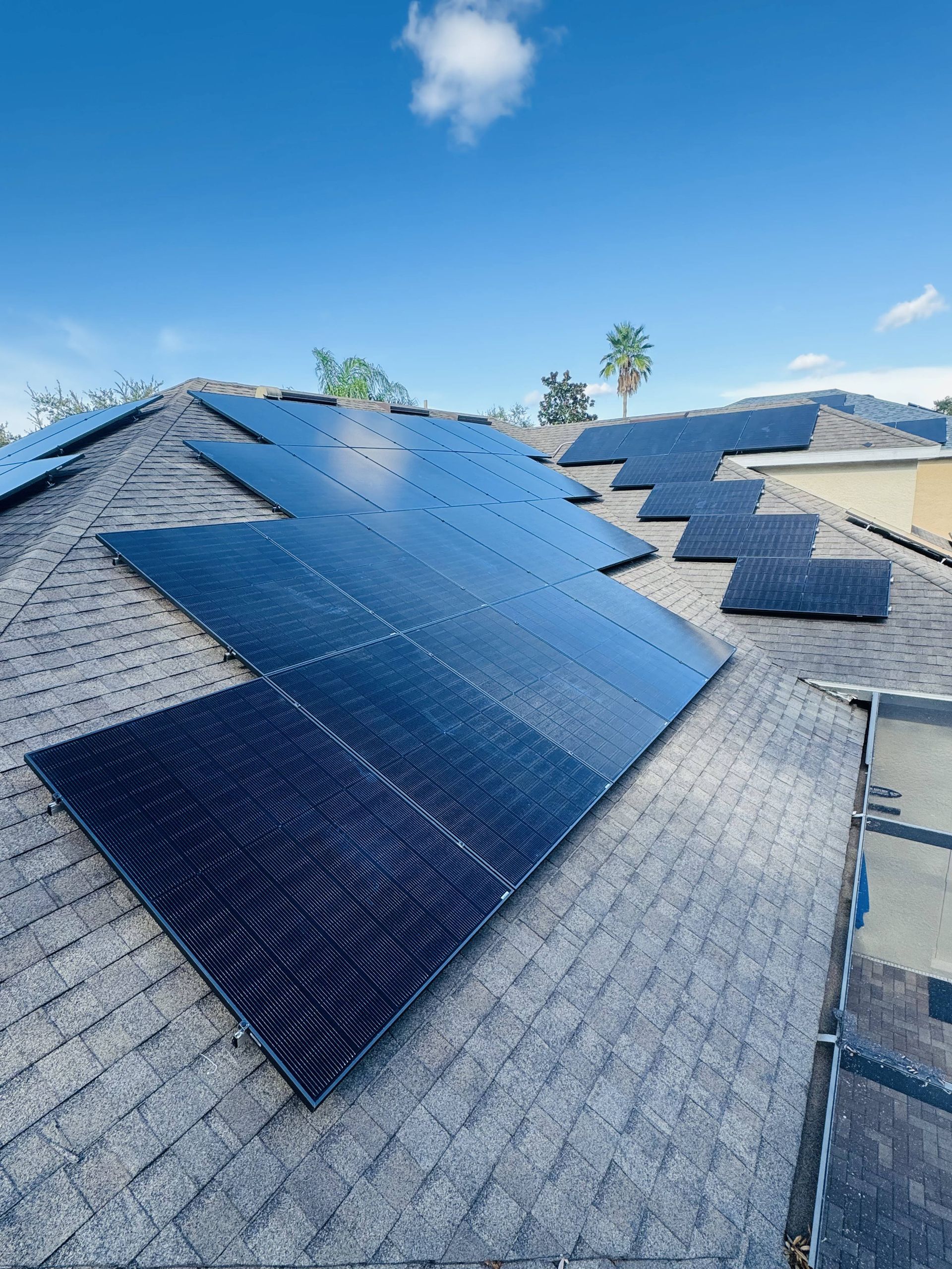 Solar panels installed on a gray shingled roof under a clear blue sky.