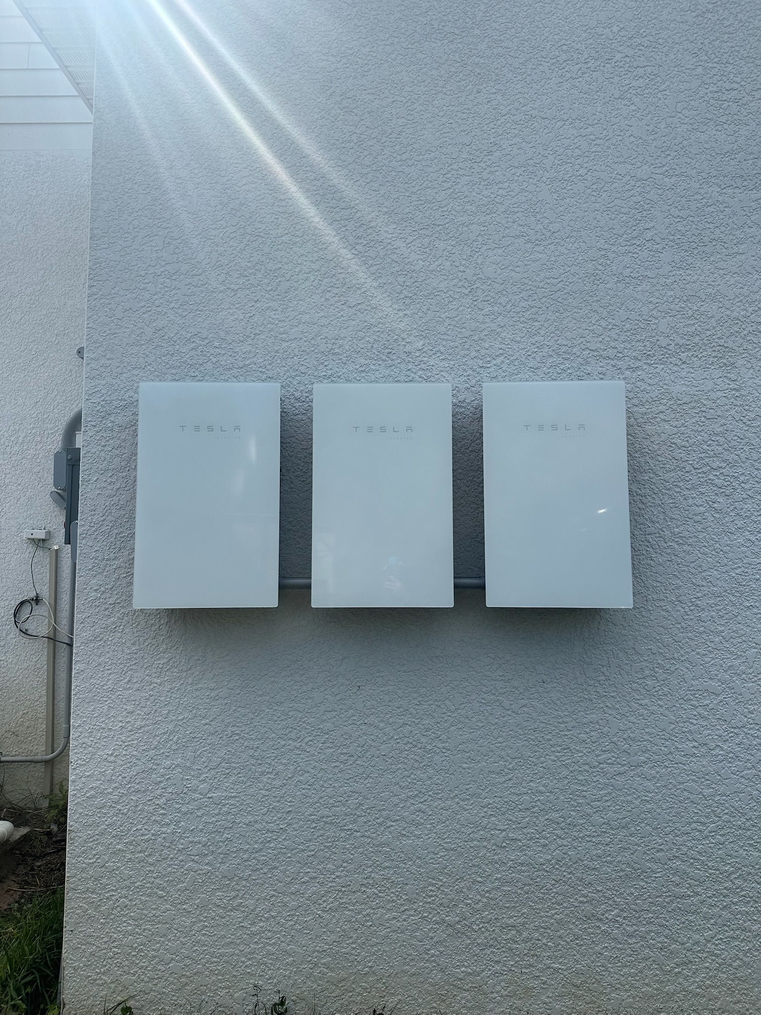 Three white wall-mounted boxes on a gray exterior wall with sunlight streaking across the top left.