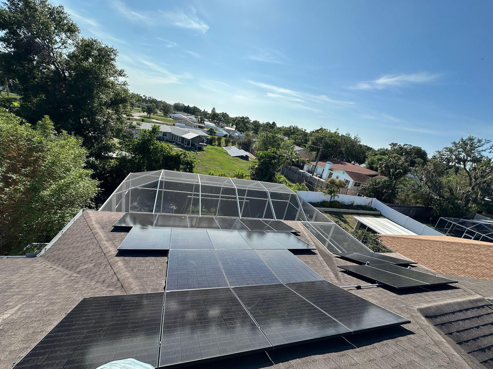 Solar panels on a rooftop overlooking a green neighborhood under a blue sky.