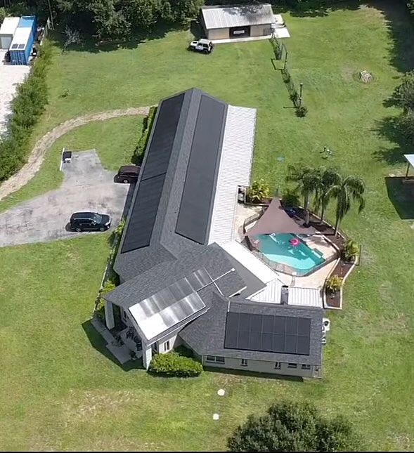 Aerial view of a gray-roofed house with a driveway, lawn, and a backyard pool.