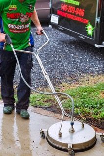 A man in a green shirt is using a pressure washer on a sidewalk.