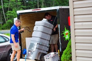 Two men are loading a large container into a trailer.