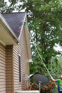 A man is cleaning the roof of a house with a long pole.