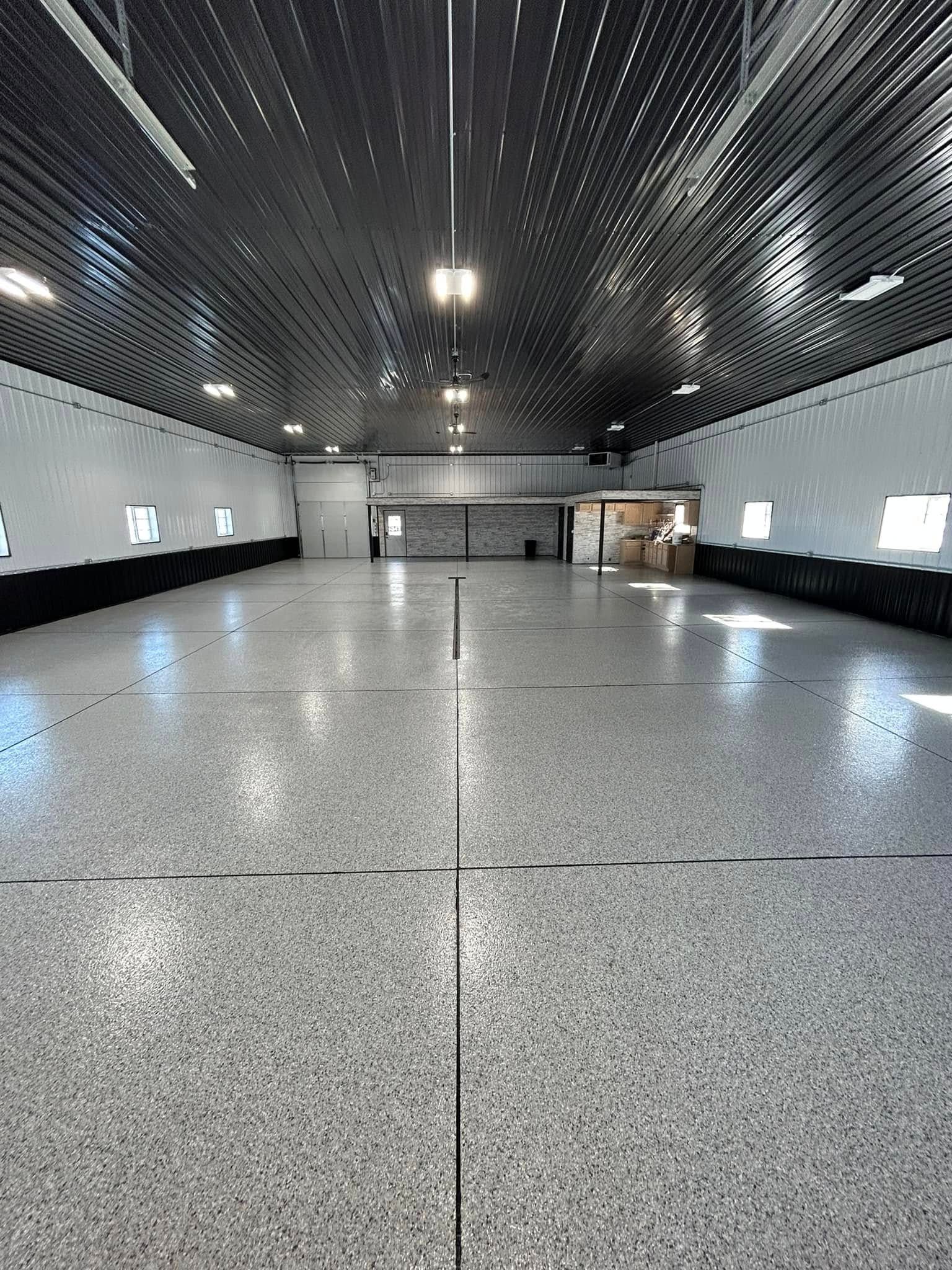 A large empty warehouse with a newly coated gray floor and a black ceiling