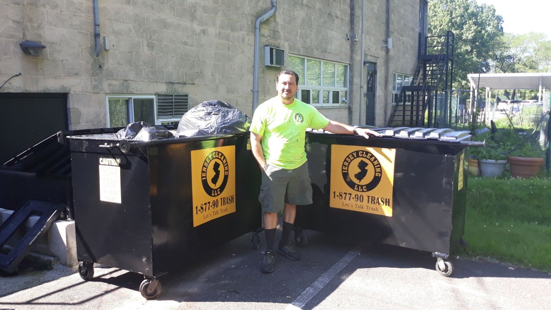 A man in a neon green shirt is standing next to a dumpster of Jersey Cleaning